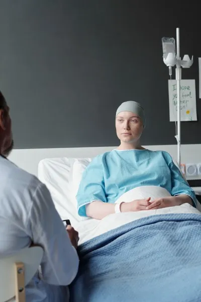 Una mujer con gorro de hospital y bata de paciente está acostada en una cama de hospital hablando con un médico, y qué es Bicnu es una posible pregunta