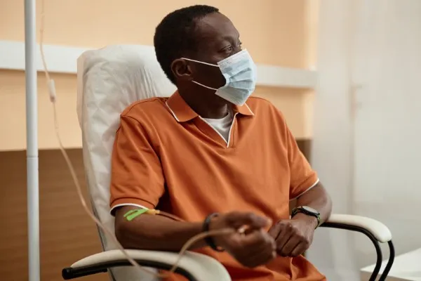 Un hombre afroamericano con mascarilla protectora recibiendo una infusión intravenosa, evocando la pregunta qué es Besponsa para su tratamiento.